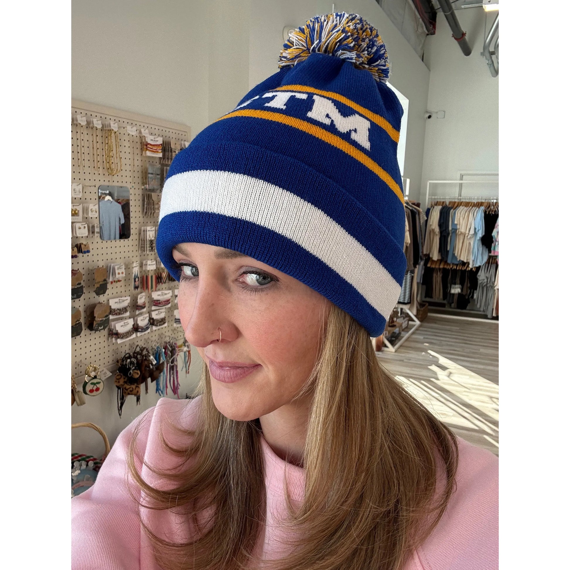 Woman wearing a blue knit beanie with pom-pom with a logo in a store setting