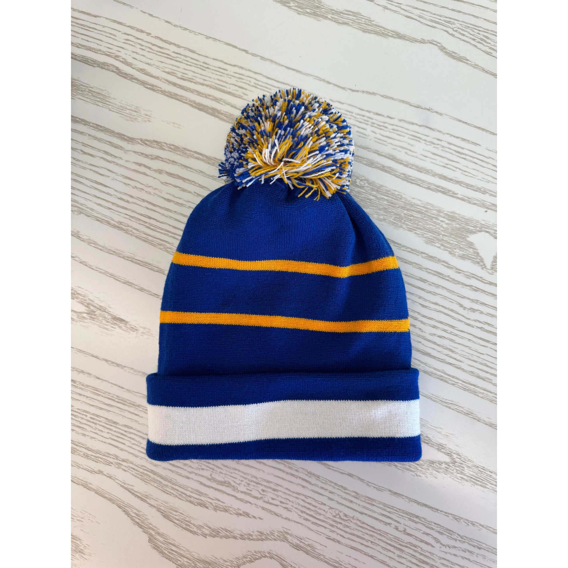 Blue beanie with yellow and white stripes and pom-pom on a wooden surface