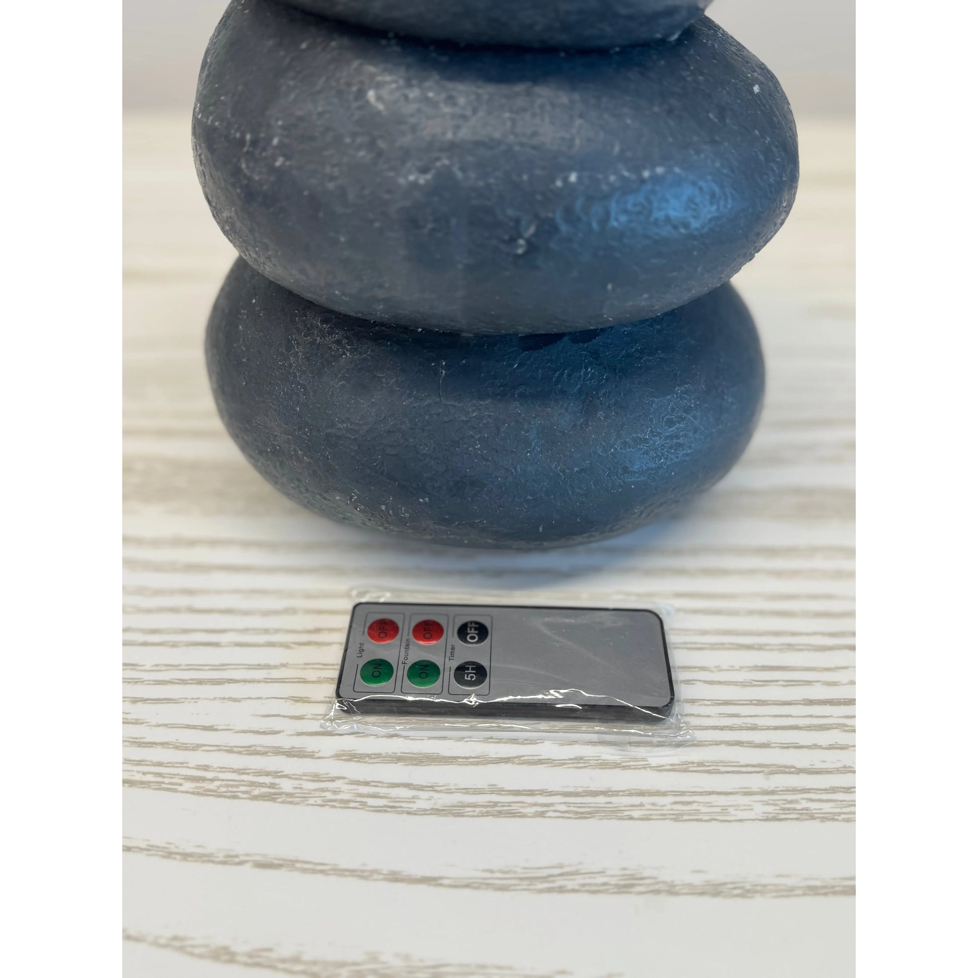 Two stacked blue stones on a light wooden surface with a small remote control in front.