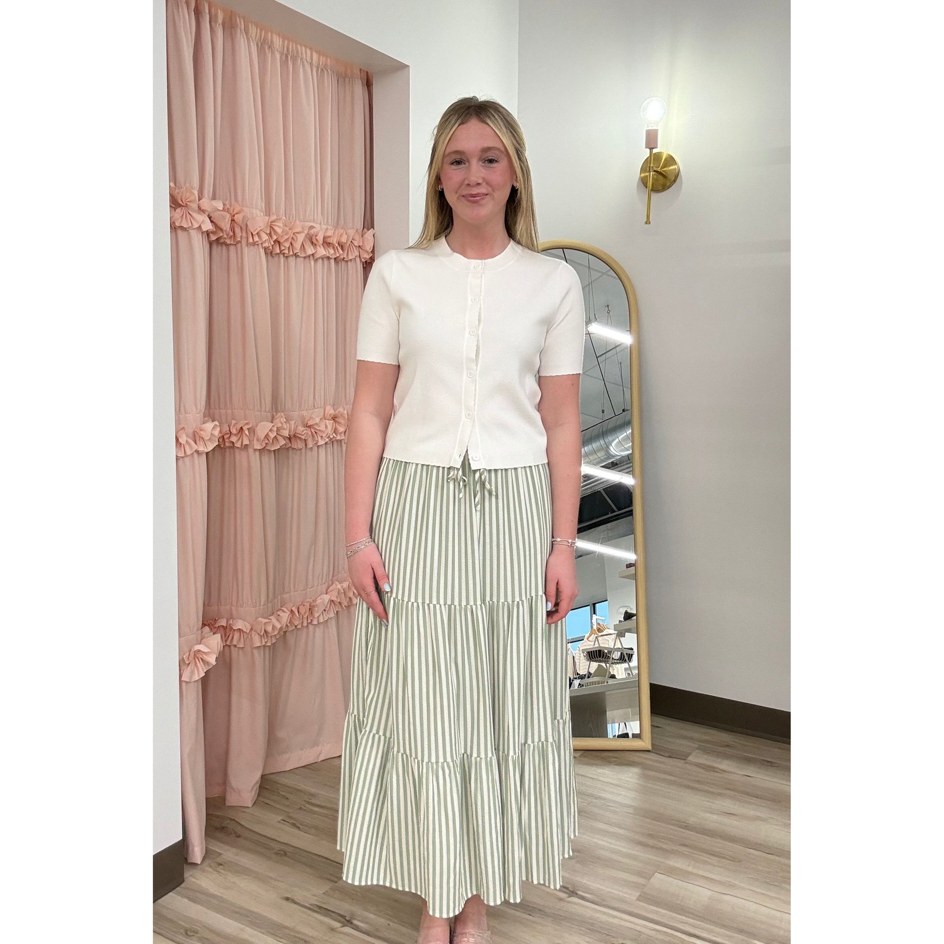 Woman standing in front of a full-length mirror wearing a white top and green striped skirt.