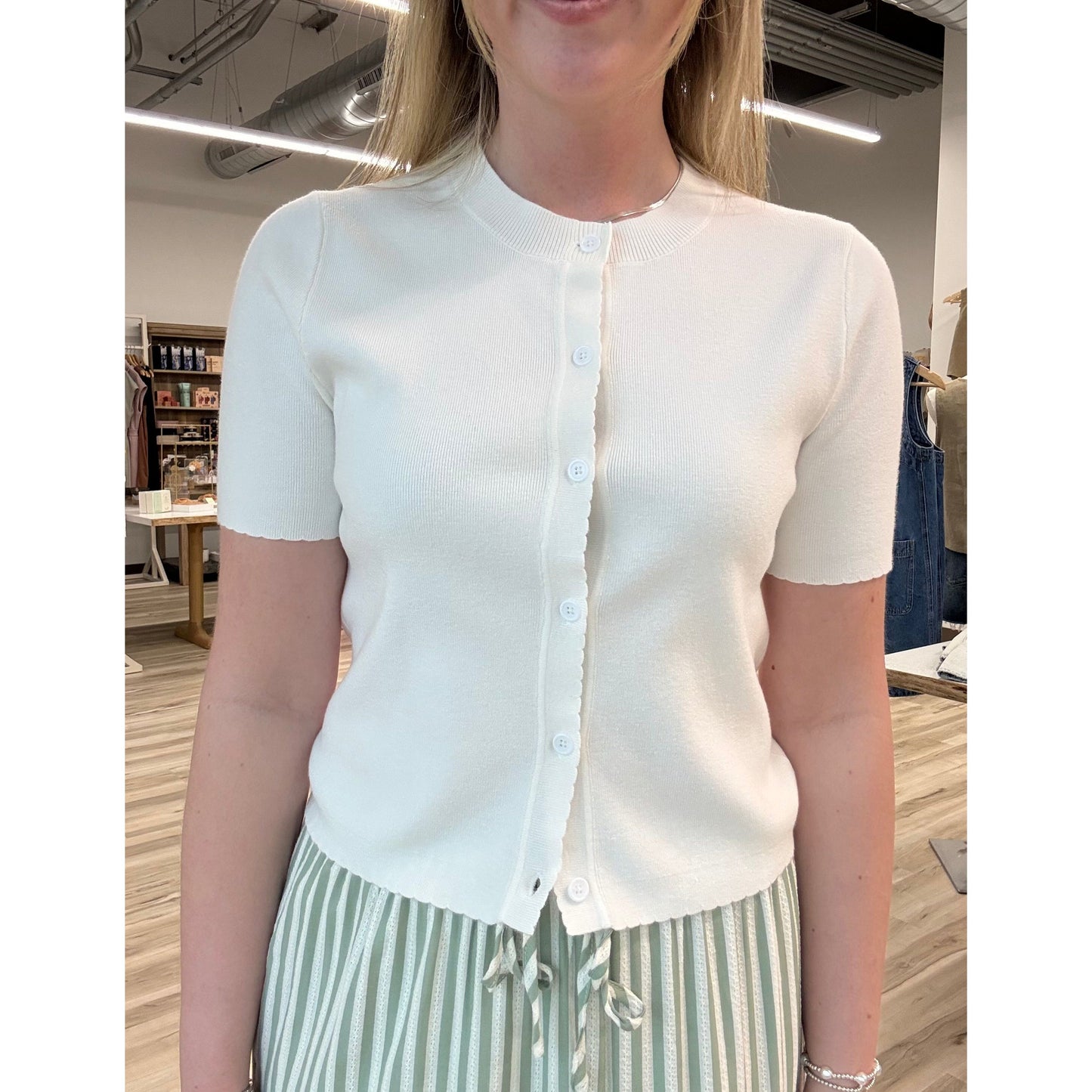 Person wearing a white short-sleeve cardigan and striped pants in an indoor setting.