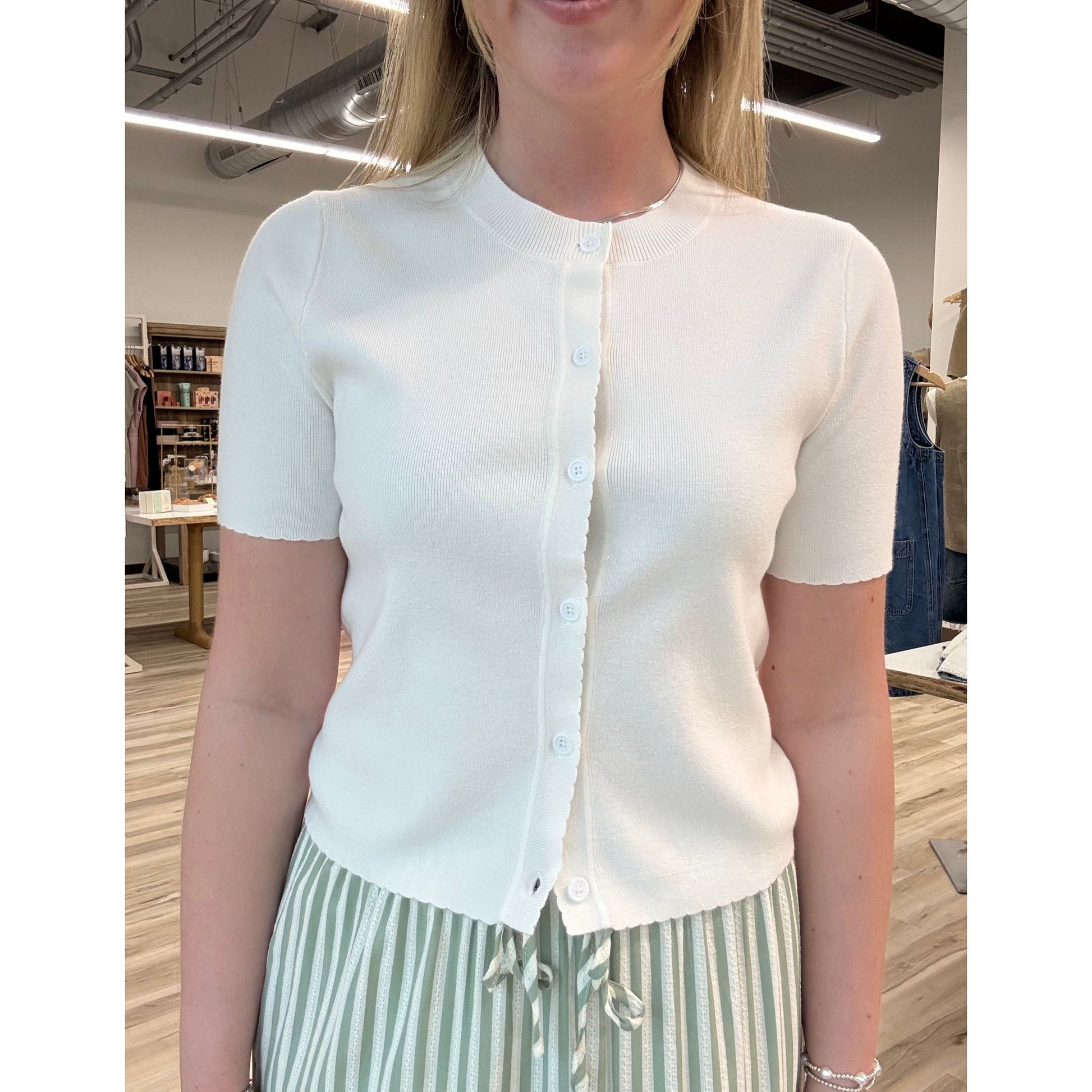 Person wearing a white short-sleeve cardigan and striped pants in an indoor setting.