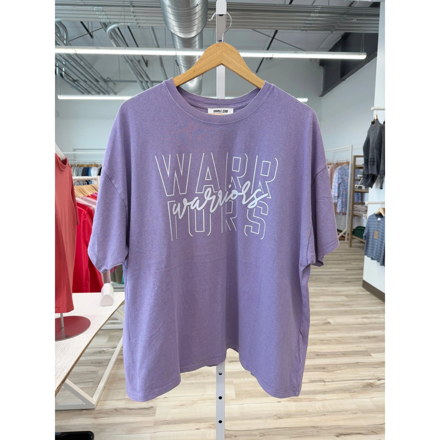 Purple t-shirt with 'Warriors' text on a hanger in a store setting