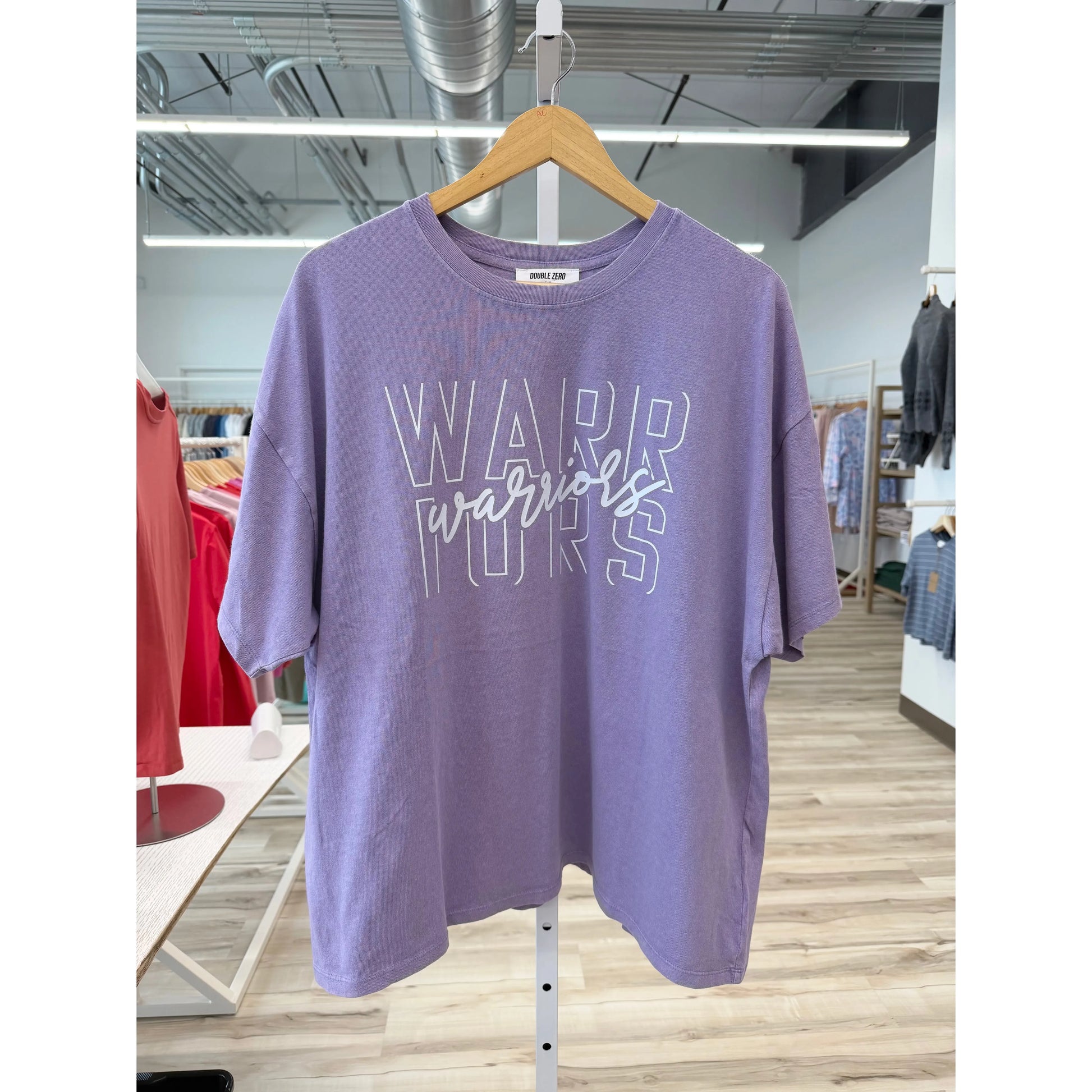 Purple t-shirt with 'Warriors' text on a hanger in a store setting