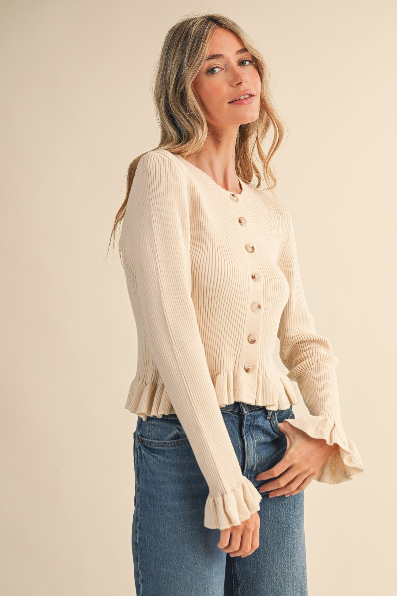 Woman wearing a beige cardigan with ruffled sleeves against a plain background