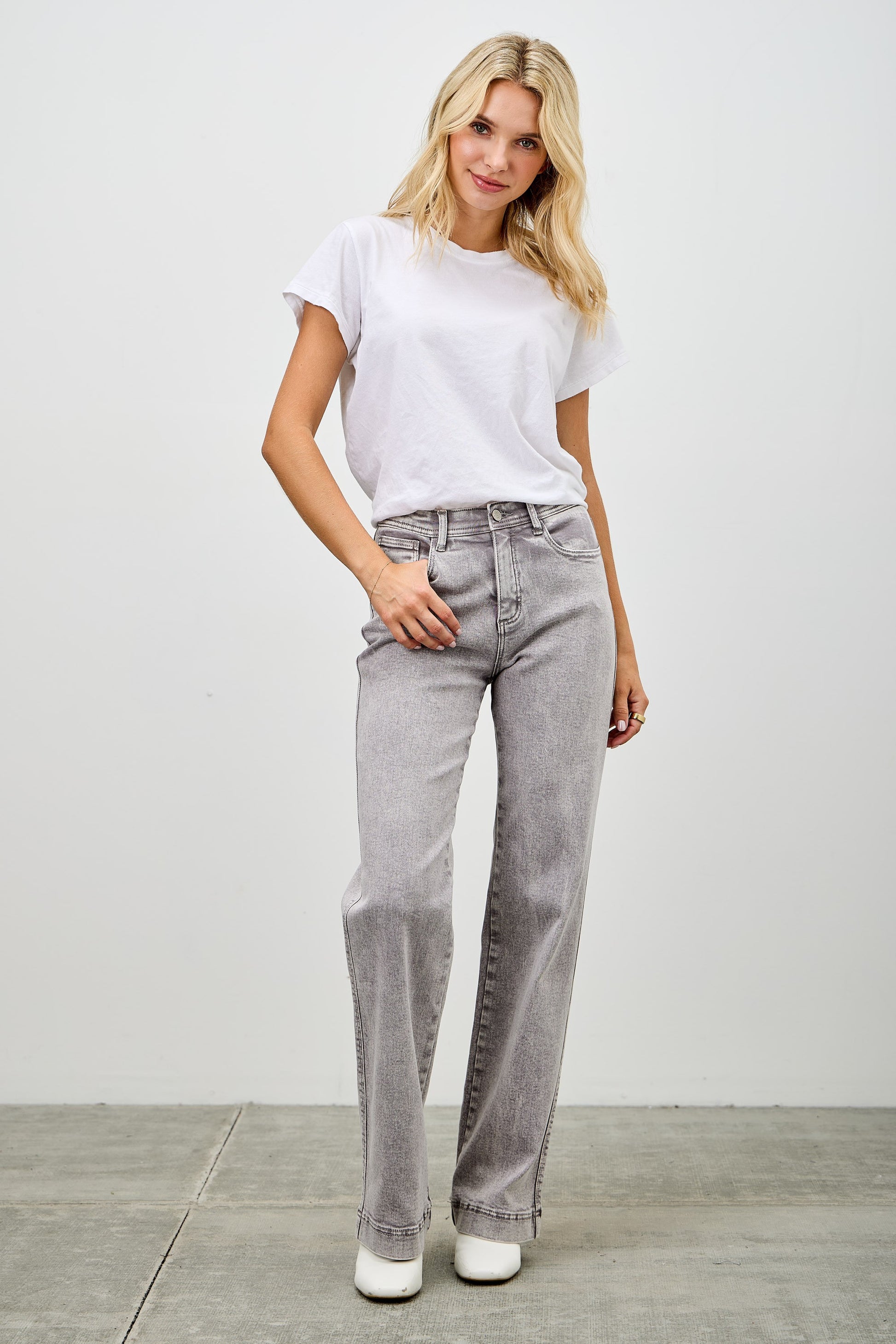Woman wearing a white t-shirt and gray jeans against a plain background