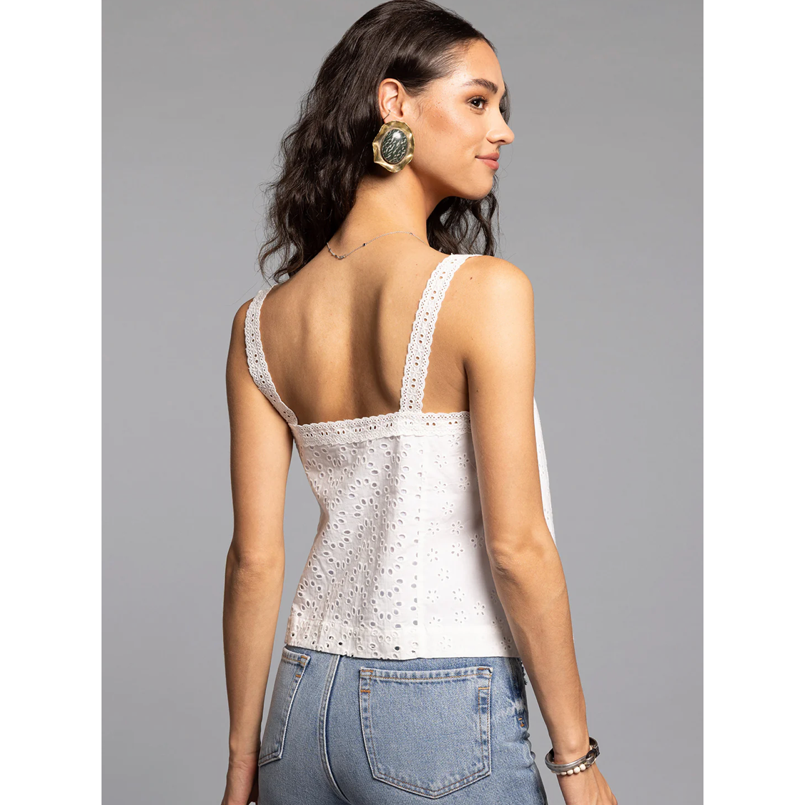 Woman wearing a white lace top and blue jeans on a gray background