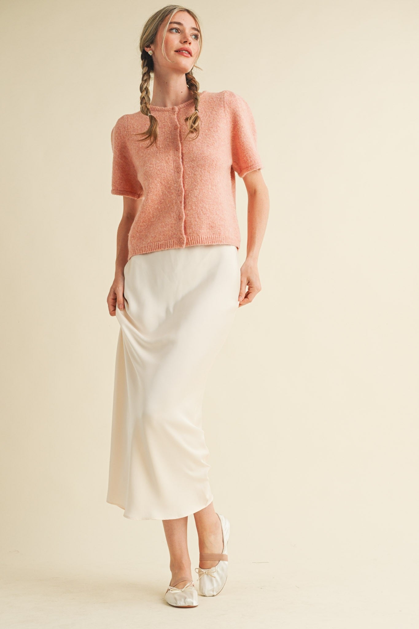 Woman wearing a pink knit top and white skirt on a beige background
