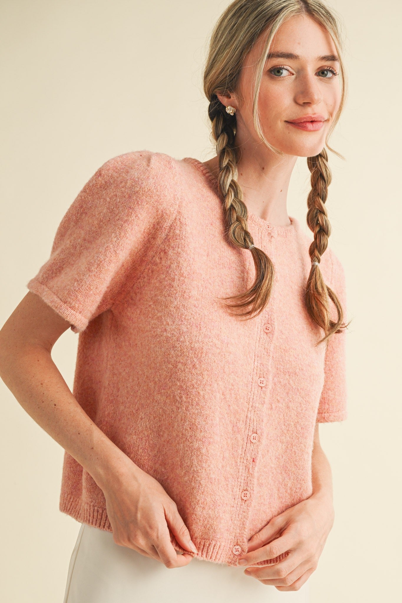 Woman wearing a pink knitted top with braided hair on a beige background