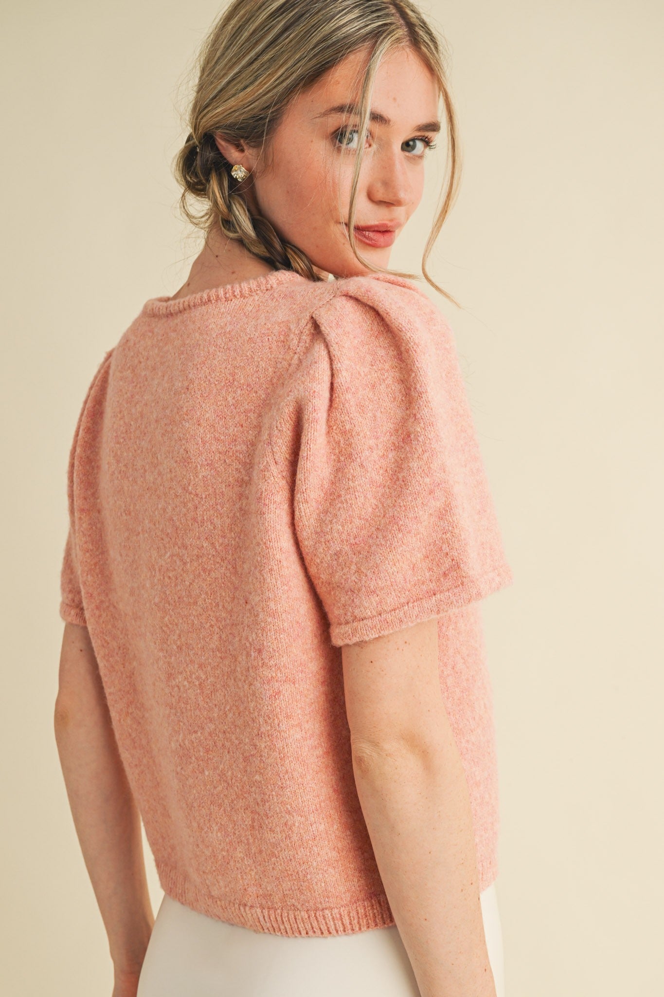 Woman wearing a pink knitted top against a beige background