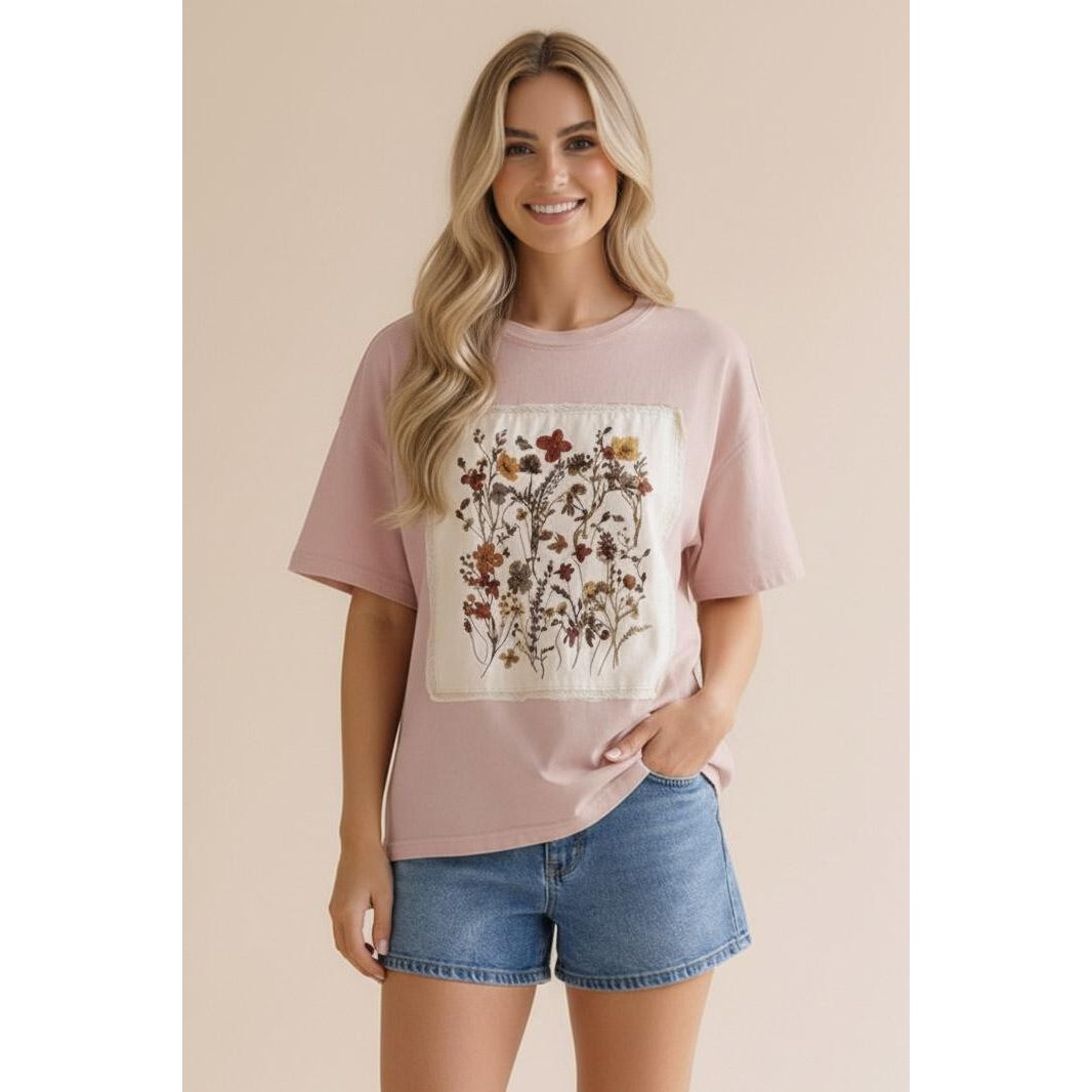 Woman wearing a pink t-shirt with a floral design and denim shorts on a beige background