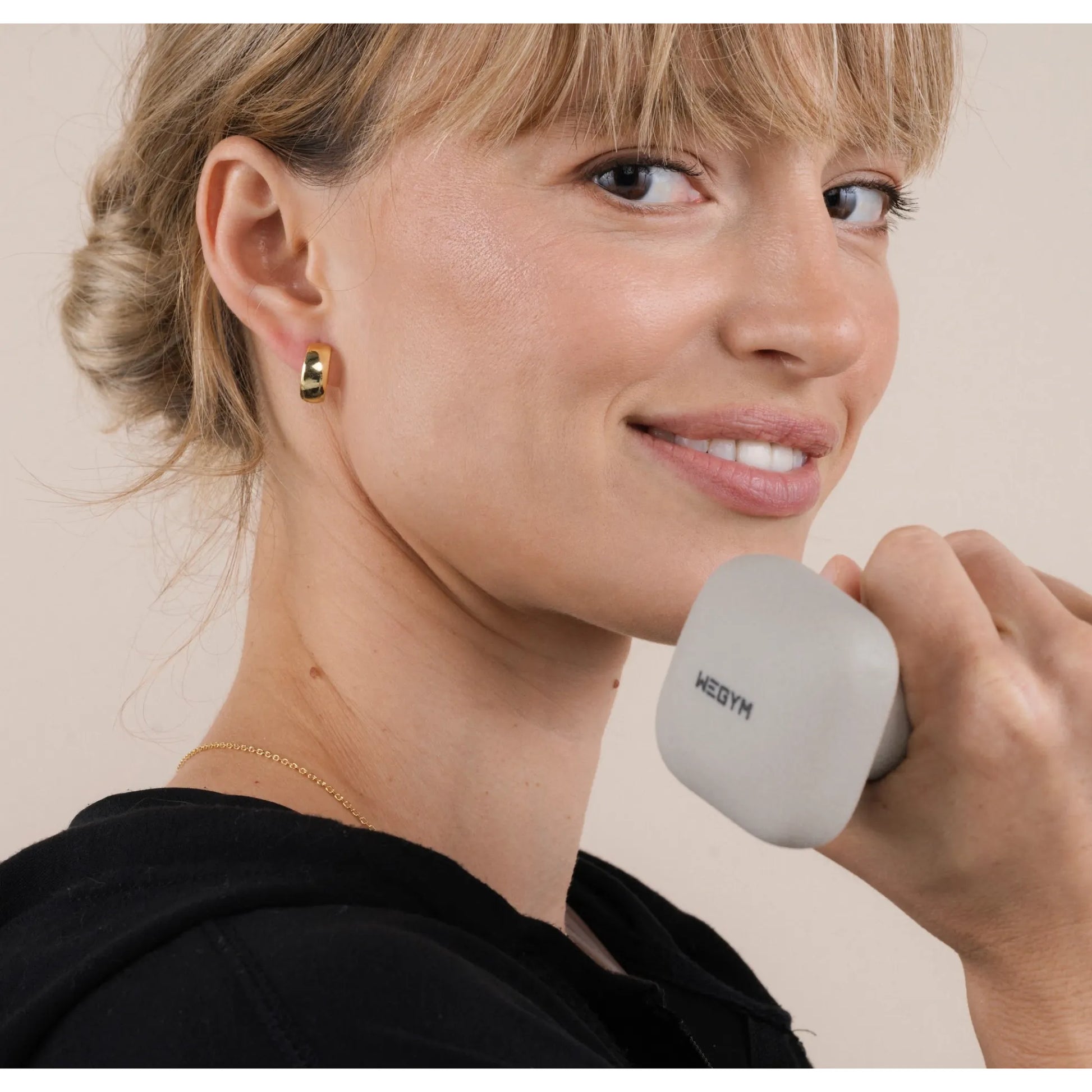 Woman holding a gray phone with 'Weym' branding, wearing gold earrings and a black top.