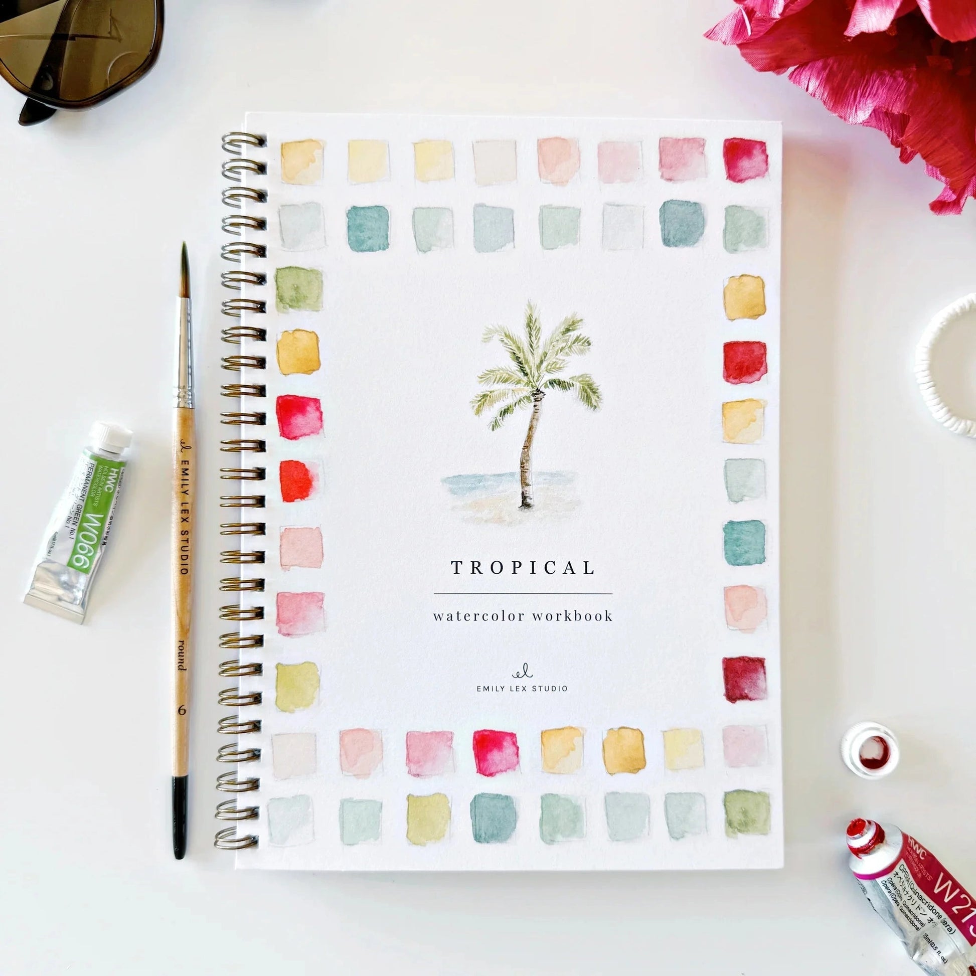 Tropical watercolor workbook with a paintbrush and paint tube on a white surface