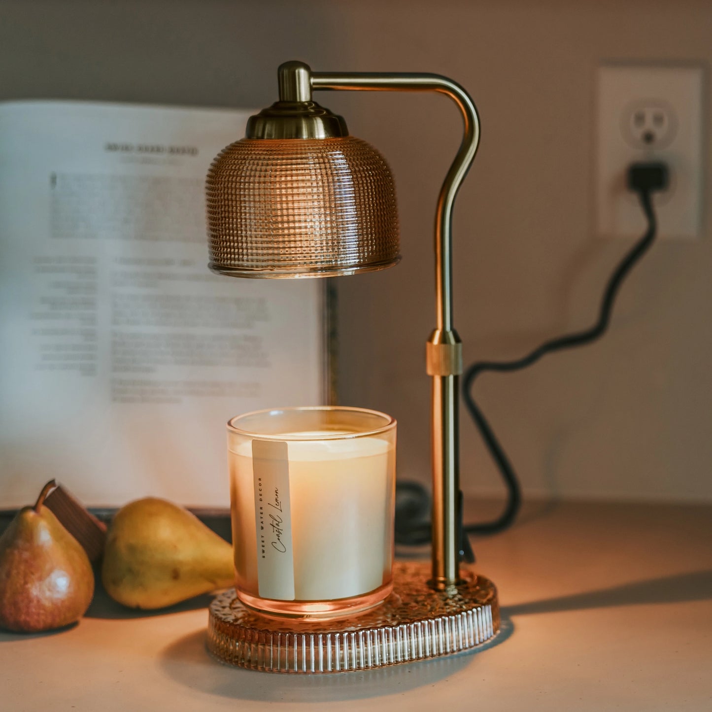Decorative lamp with a candle on a table next to pears and a blurred book
