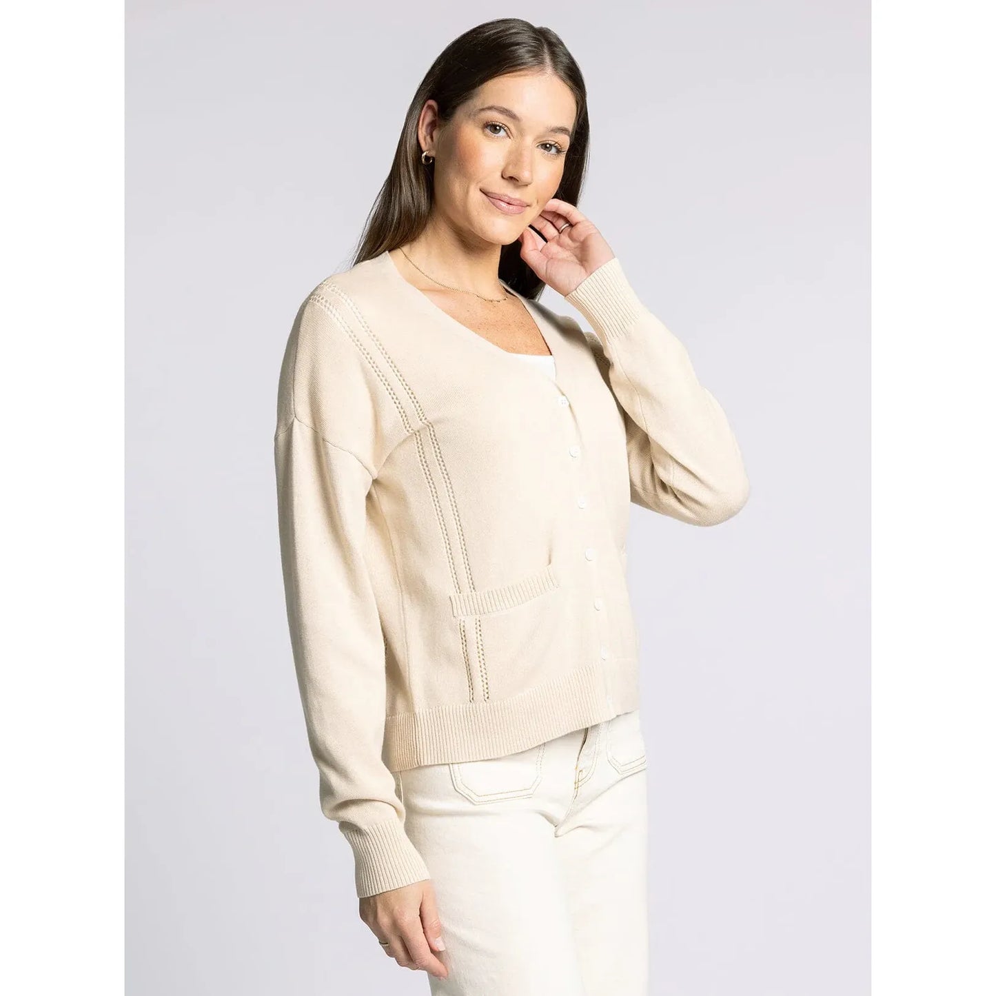 Woman wearing a beige sweater and white pants against a light gray background