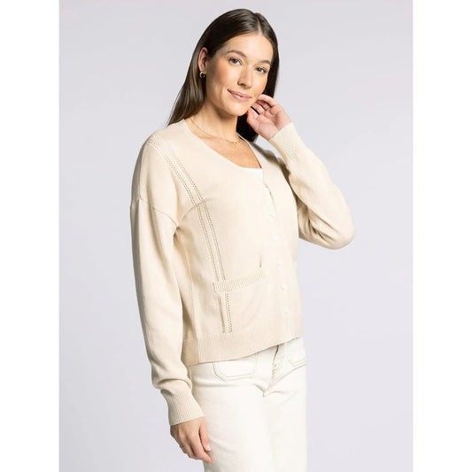 Woman wearing a beige sweater and white pants against a light gray background