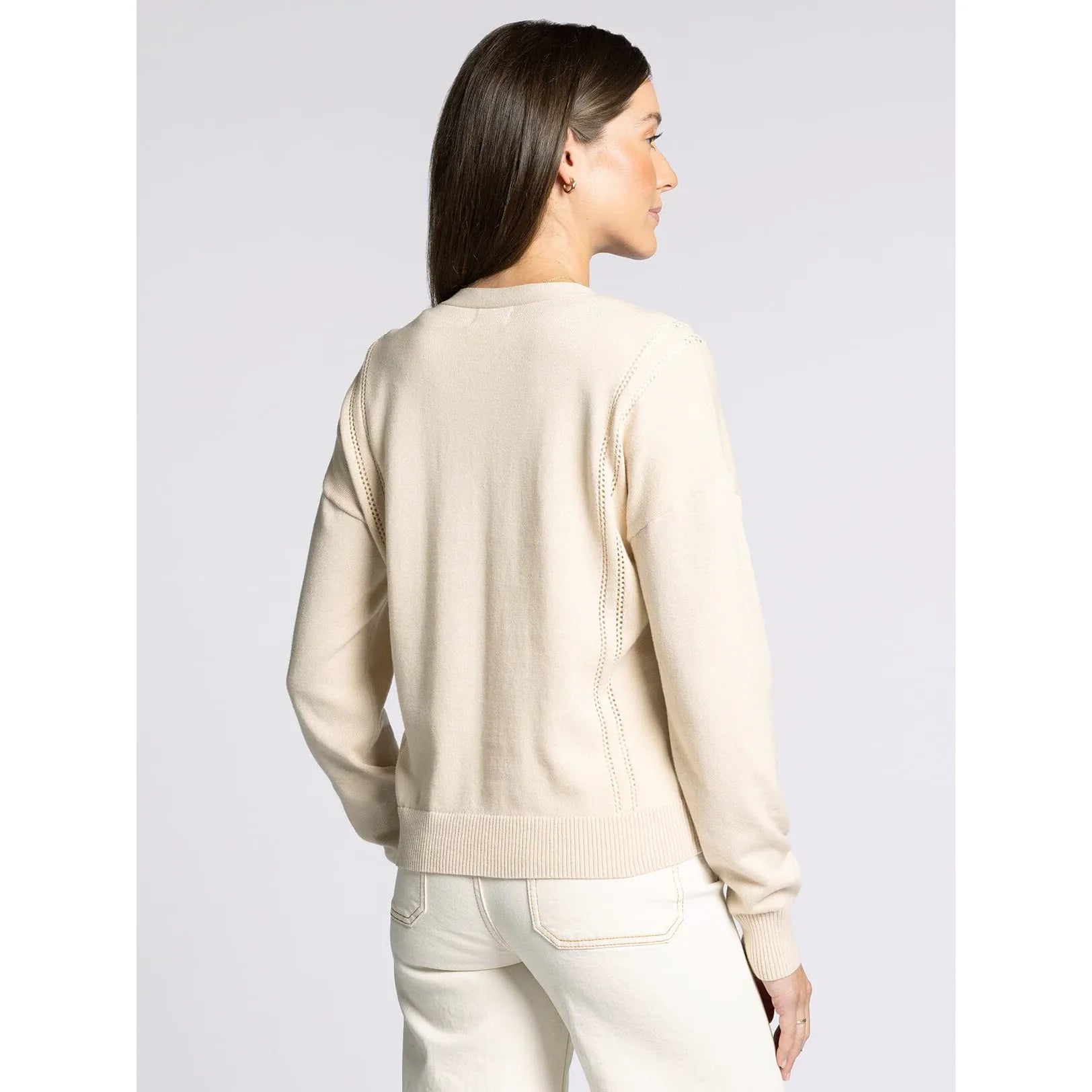 Woman wearing a beige sweater and white pants on a light gray background