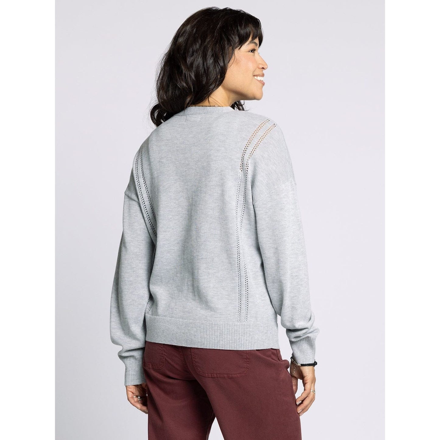 Woman wearing a light gray sweater with decorative stitching on a plain background