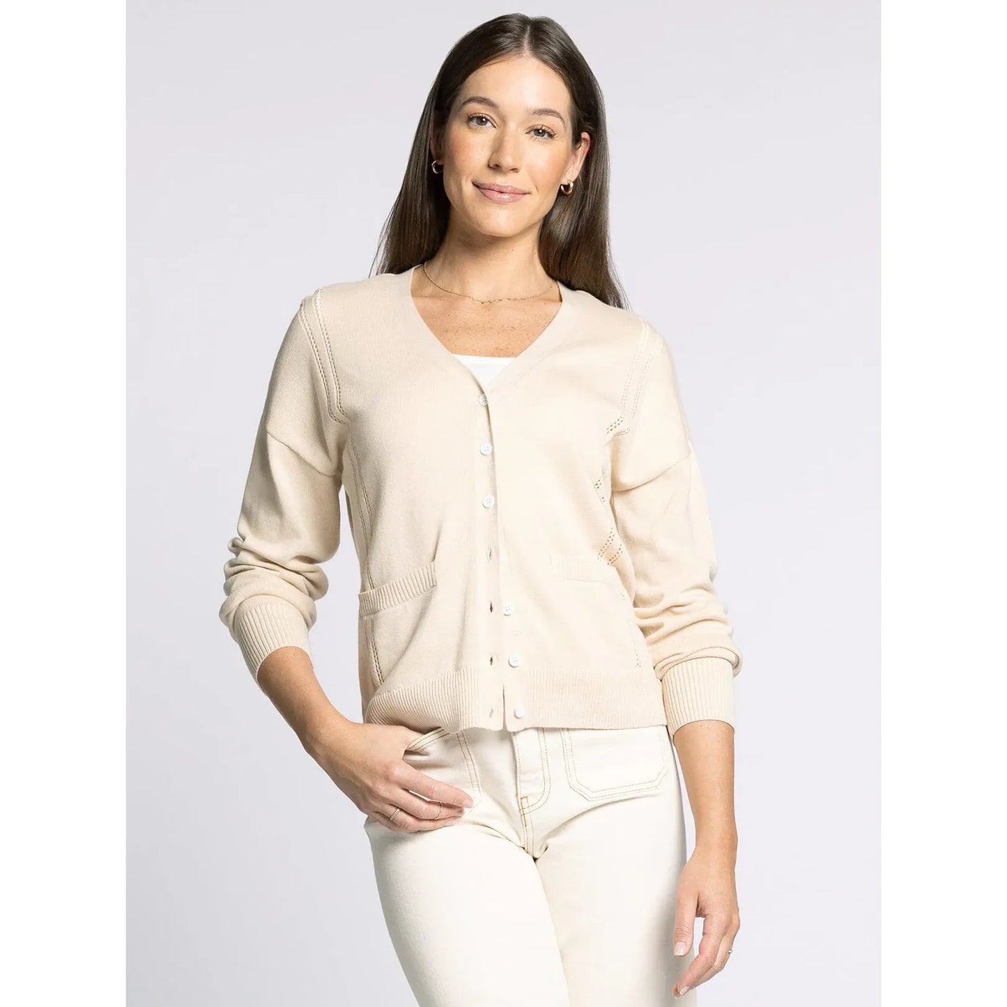Woman wearing a beige cardigan and white pants on a light gray background