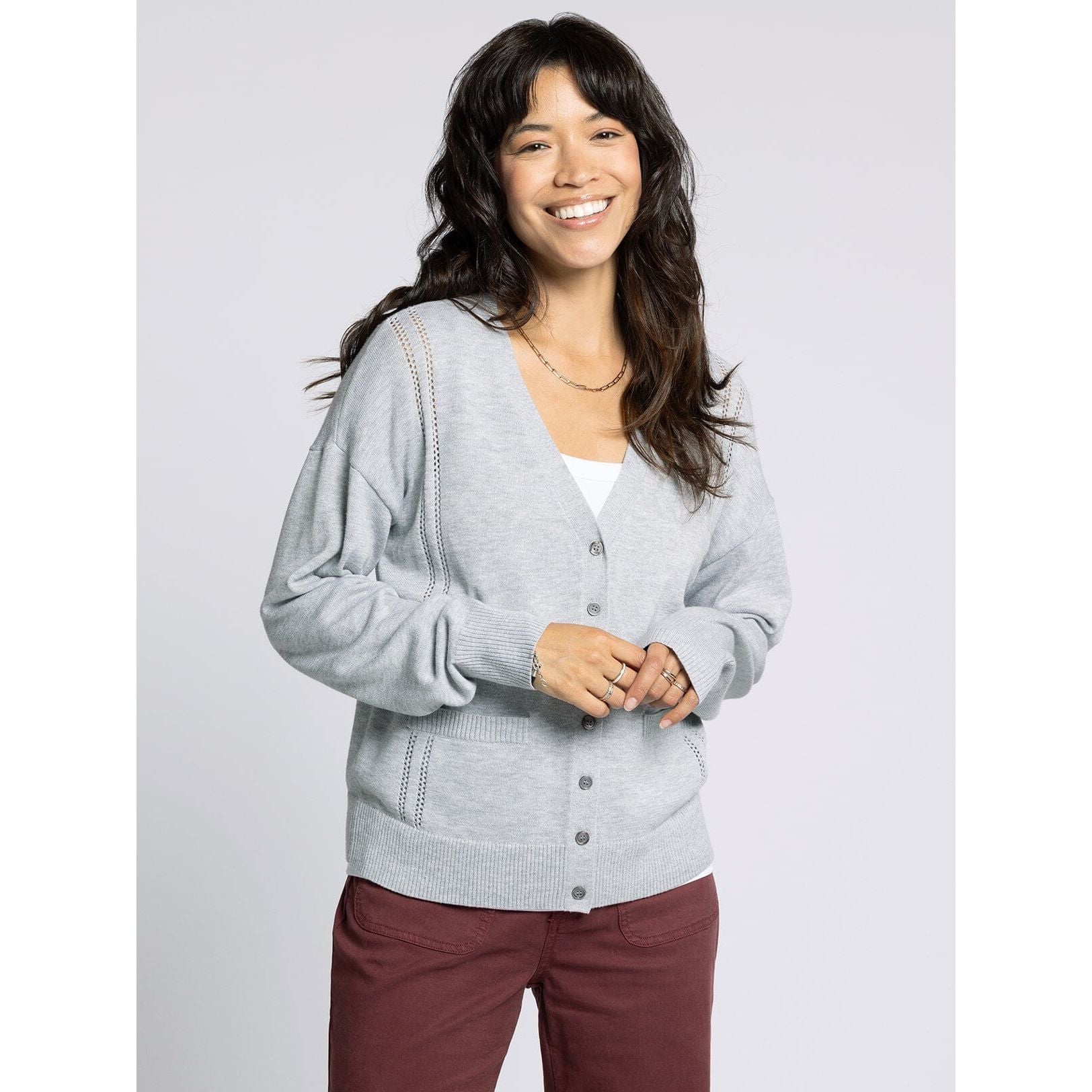 Woman wearing a gray cardigan over a white top with maroon pants on a light gray background