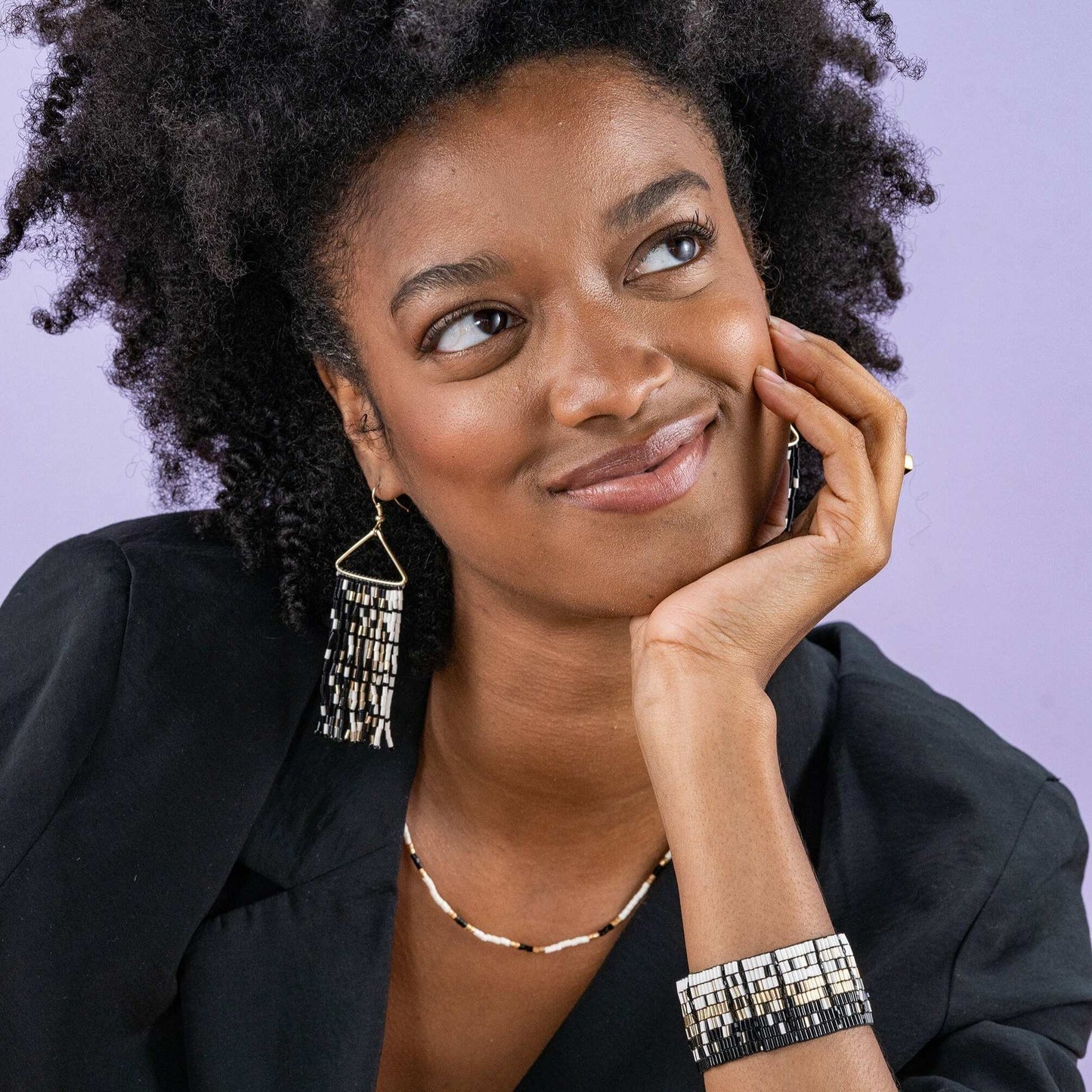 Woman wearing earrings, necklace, and bracelet against a purple background