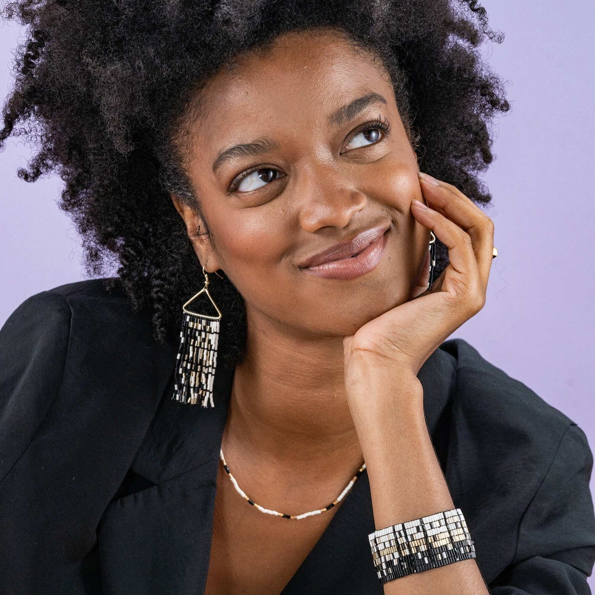 Woman wearing earrings, necklace, and bracelet against a purple background