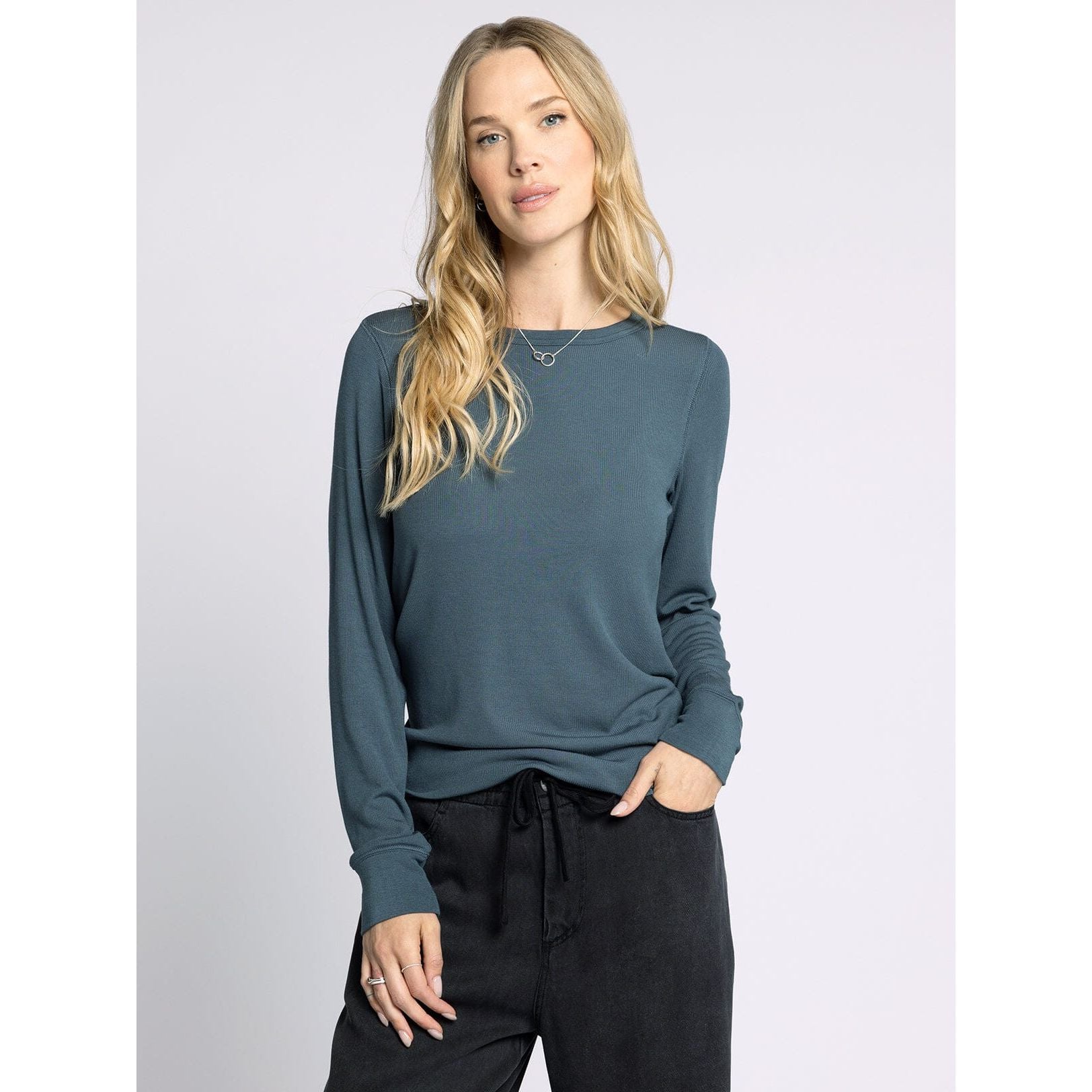 Woman wearing a teal long-sleeve top and black pants on a light gray background